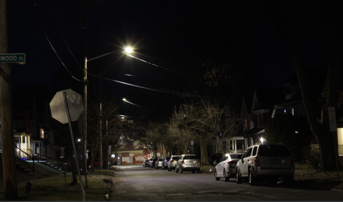 A residential street at night, illuminated by a row of streetlights.
