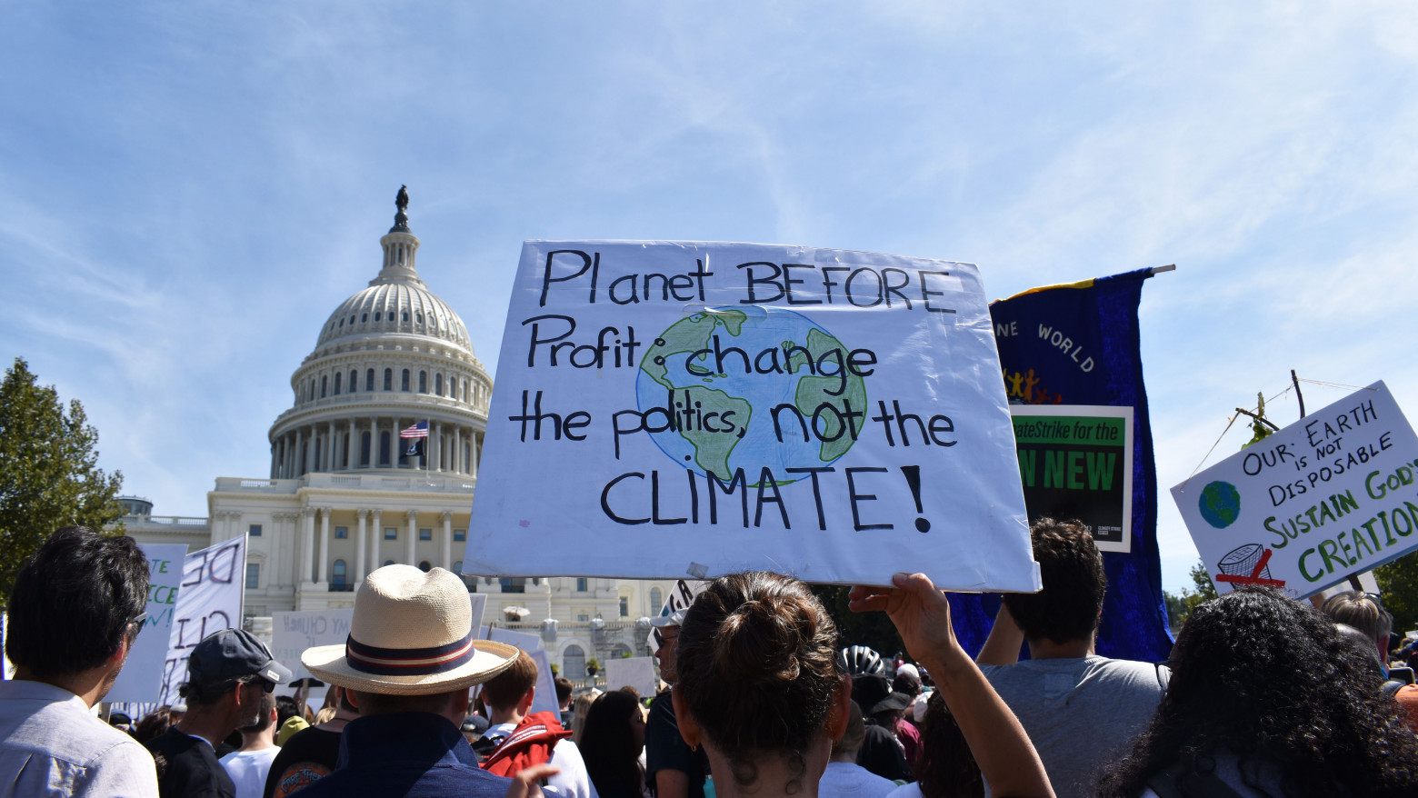 In a crowd of people in front of the Capitol building in Washington, D.C., a sign reads: "Planet BEFORE Profit: change the politics, not the CLIMATE!"