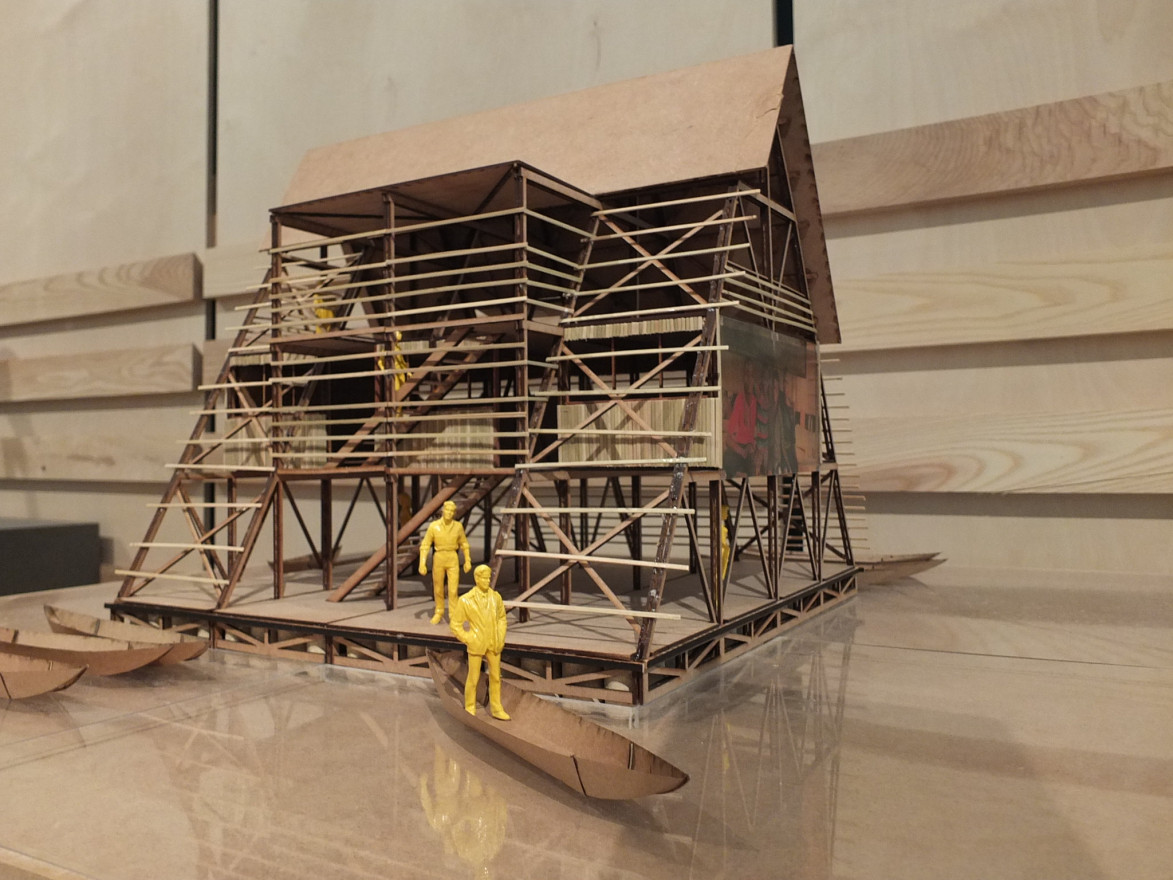 A prototype wooden model of the architect's triangular structure, and features scaled down human figures, and boats. The sides of the building are open to allow the viewer to peer inside.