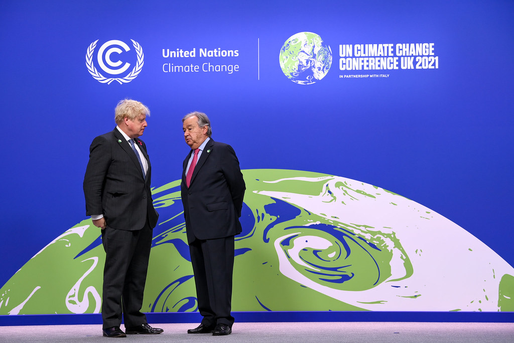 Two men in suits talk to one another in front a blue wall with green and white United nation Climate Change graphics.