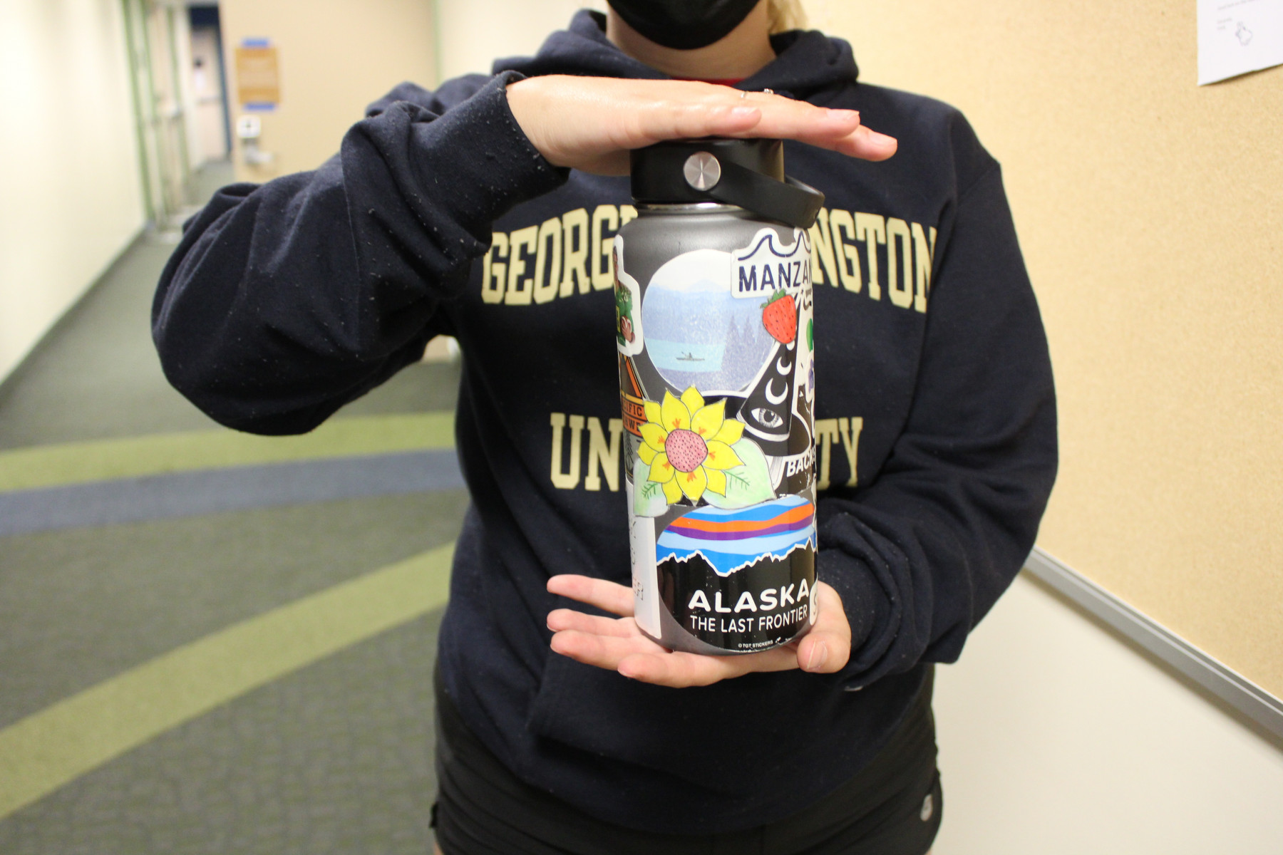 A person in a navy George Washington University sweatshirt, head not pictured, holds a reusable plastic water bottle with many stickers.