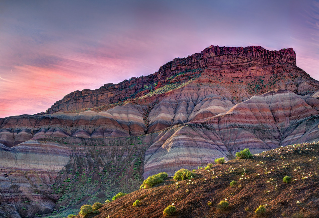 A striated canyon under a sunrise sky in shades of purple and pink.