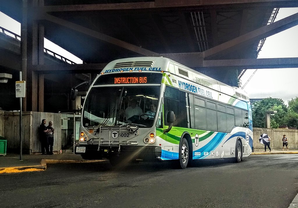 A white, green and blue bus with text that reads "Hydrogen Fuel Cell" parked in a terminal.