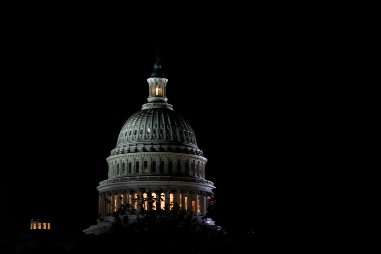 The white dome of the US Capital building is illuminated under a dark sky.