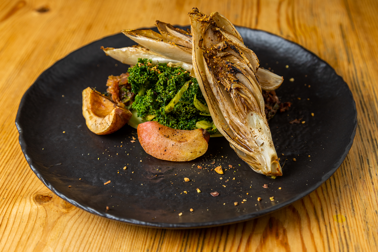 A dark plate sits on a wooden table holding artfully placed plant-based food.