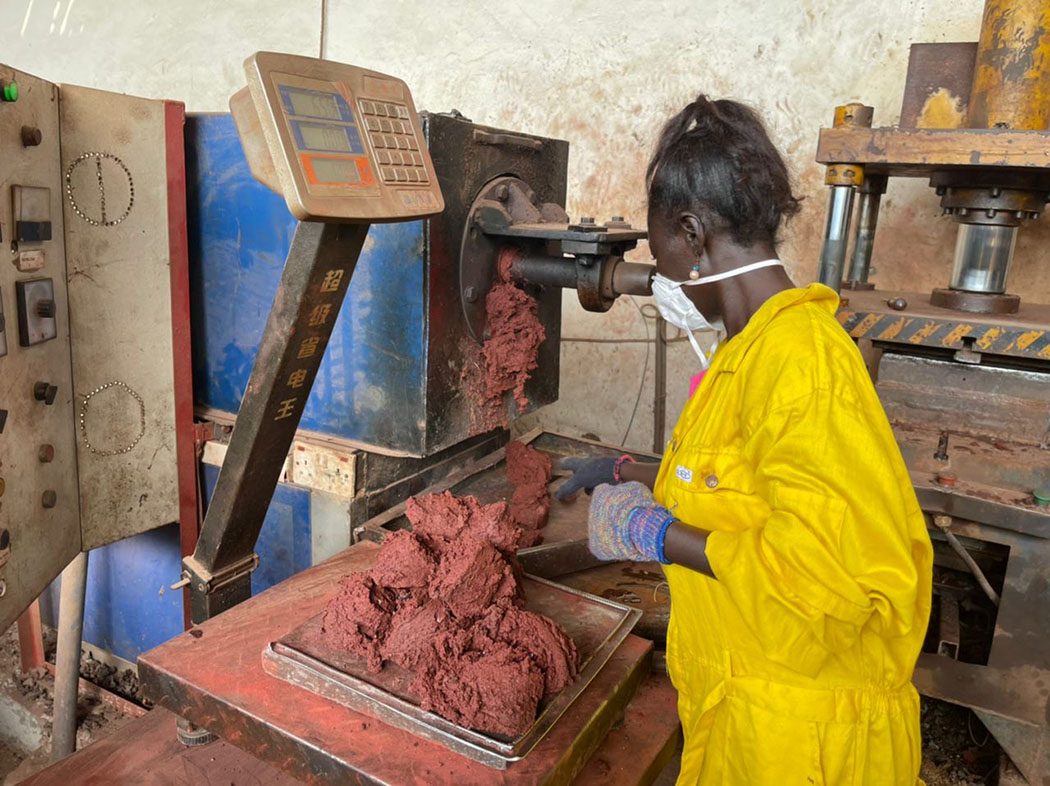 A woman wearing yellow works at a machine with what looks like a red paste