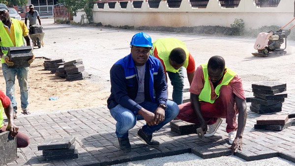 Nelson Boateng crouches on the ground with workers, laying grey, flat NetPlast pavers
