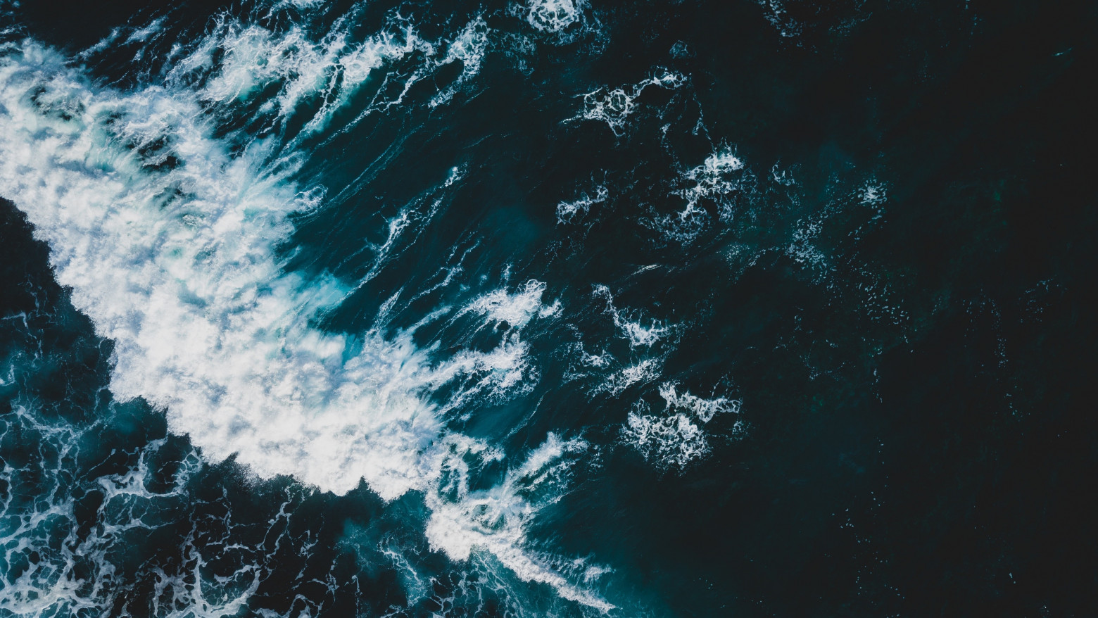 A wave breaks on a dark blue ocean, unleashing a cascade of white foam.