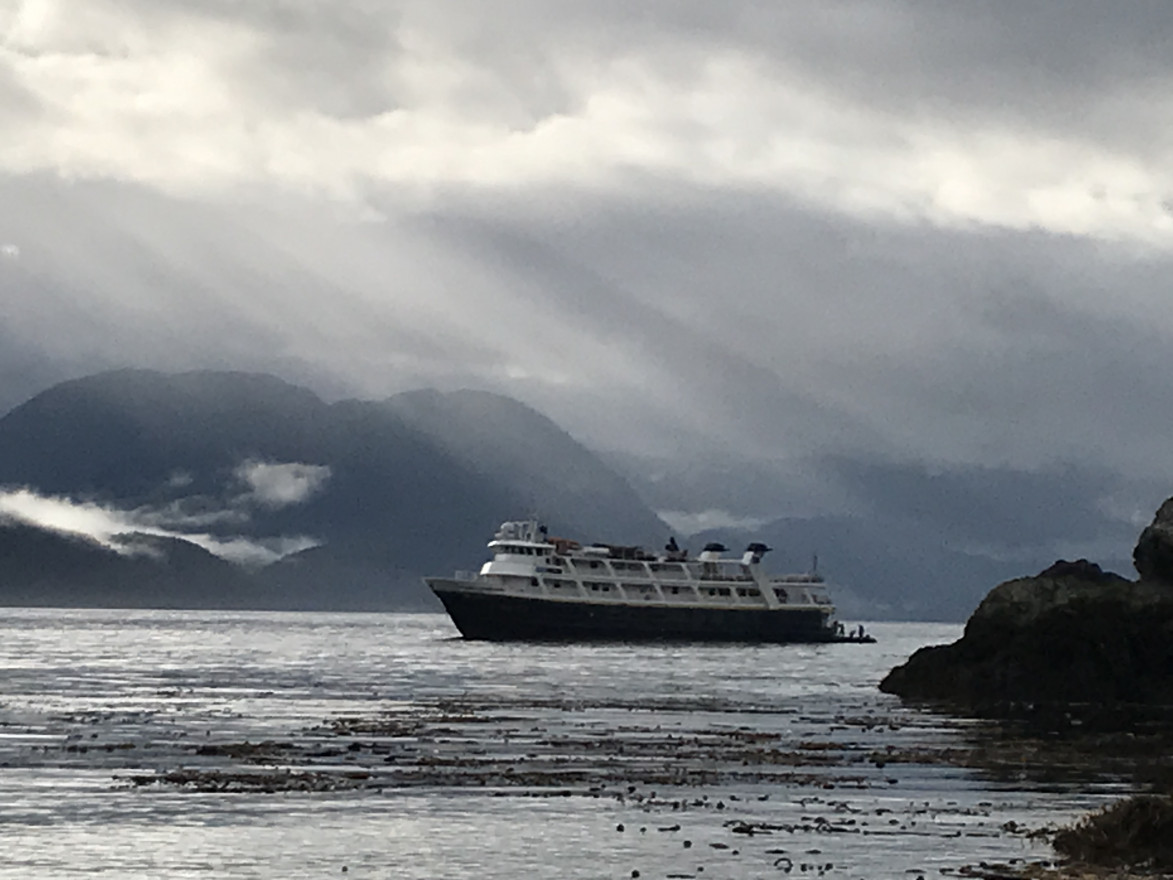 A cruise ship chugs along a bay in Alaska with rays of light beating down from the sky. 
