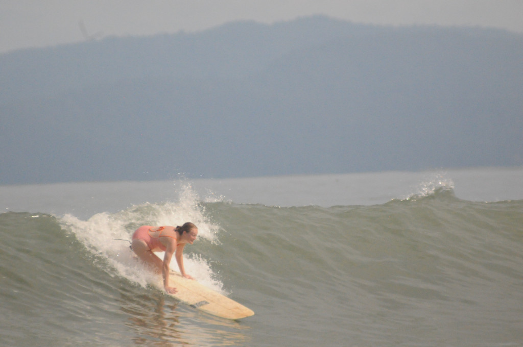 The author kneels on her surfboard while riding a wave.