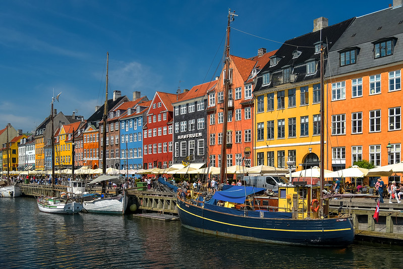 A row of colorful houses along a picturesque canal in Denmark. Sailboats are docked along the canal edge. 