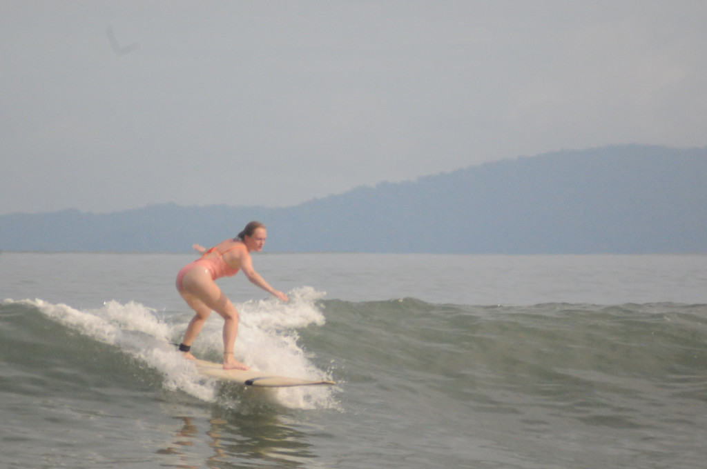 The author stands on her surfboard while riding a wave.