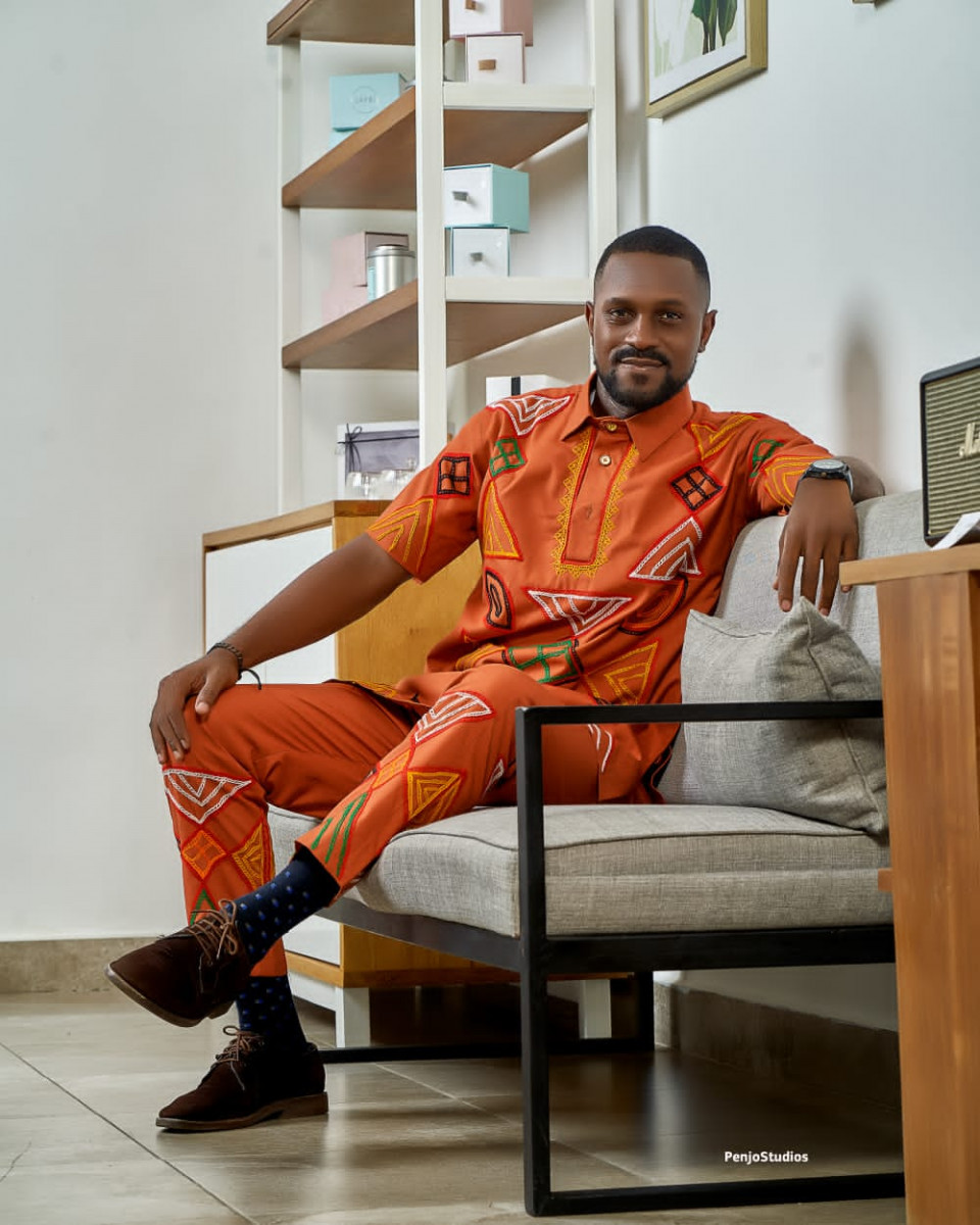 A man poses while wearing a bright orange shirt and pants by fashion designer, Ngwane Liz..