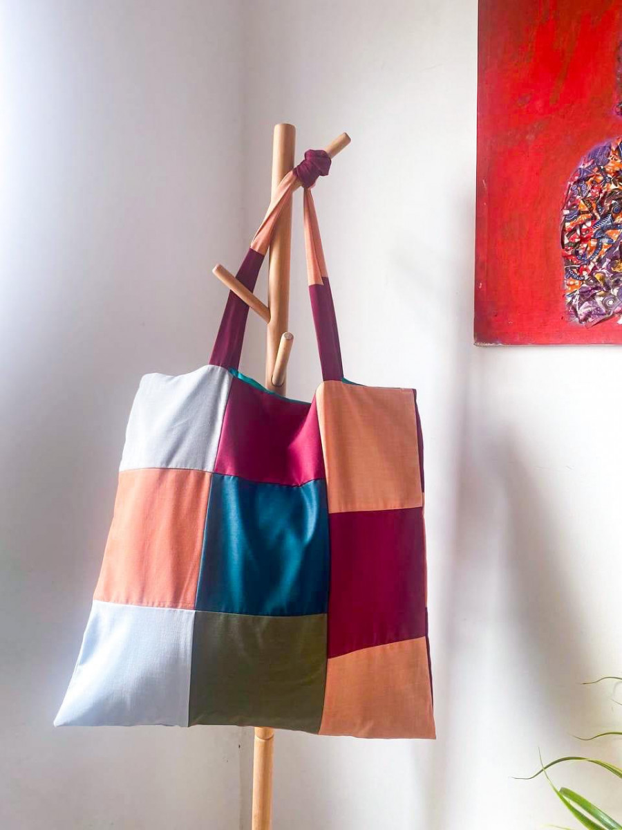 A tote bag made of recycled patches hangs from a coat hanger. 