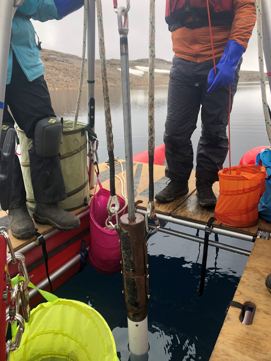 A group of Ph.D. students lift a sediment core out of the water while standing on a raft in the middle of a lake.