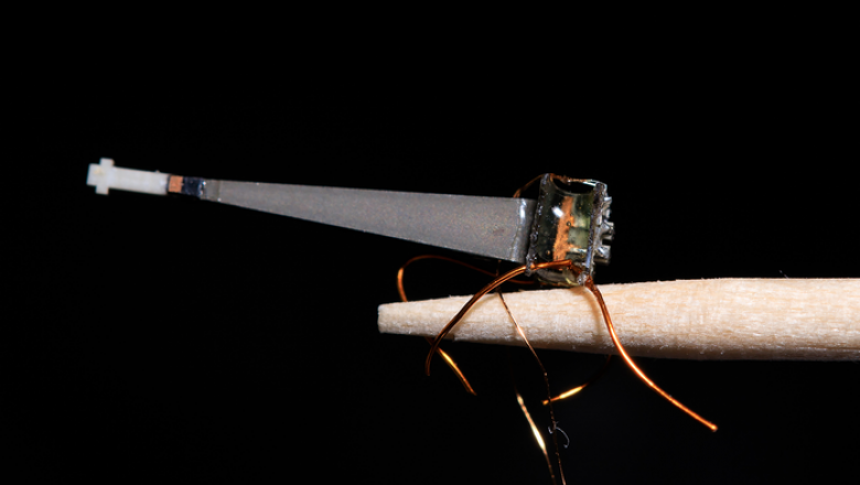 An extreme close up of a tiny robotic bee perched on the end of a toothpick.