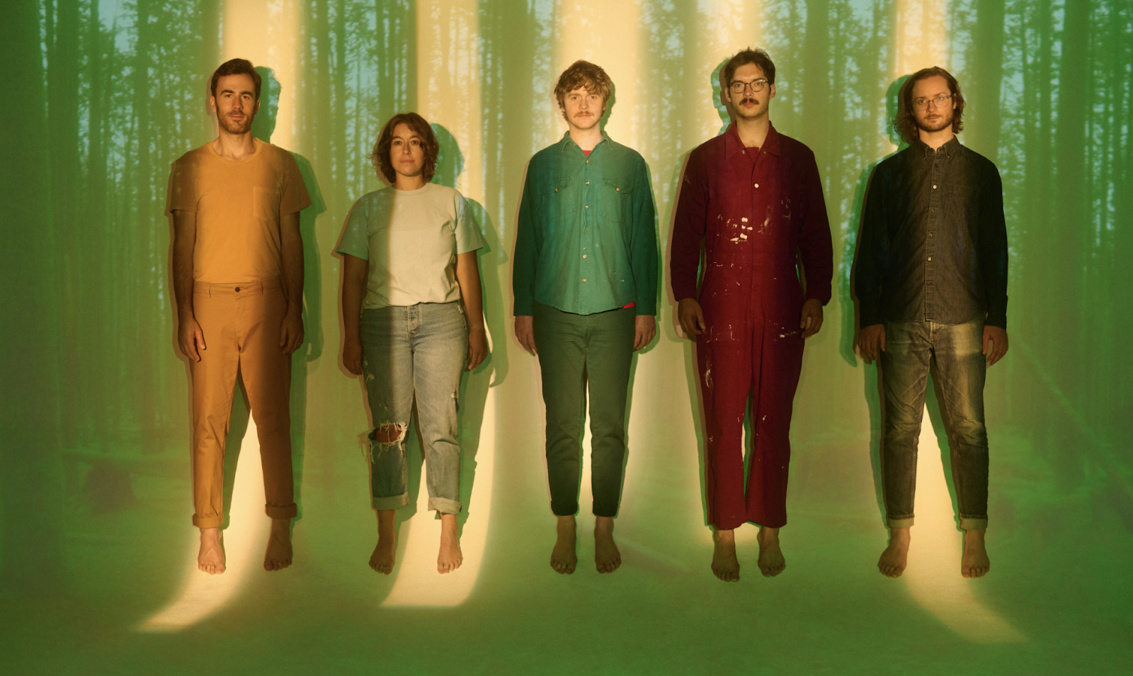 The five members of Pinegrove stand, directly facing the camera, against a wall with a forest projected upon it.