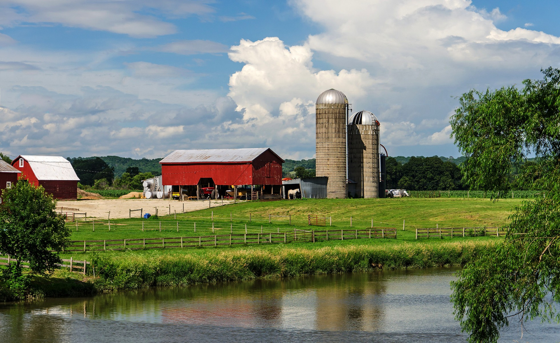 A picturesque farm with a red barn and silos on the banks of a small river. 