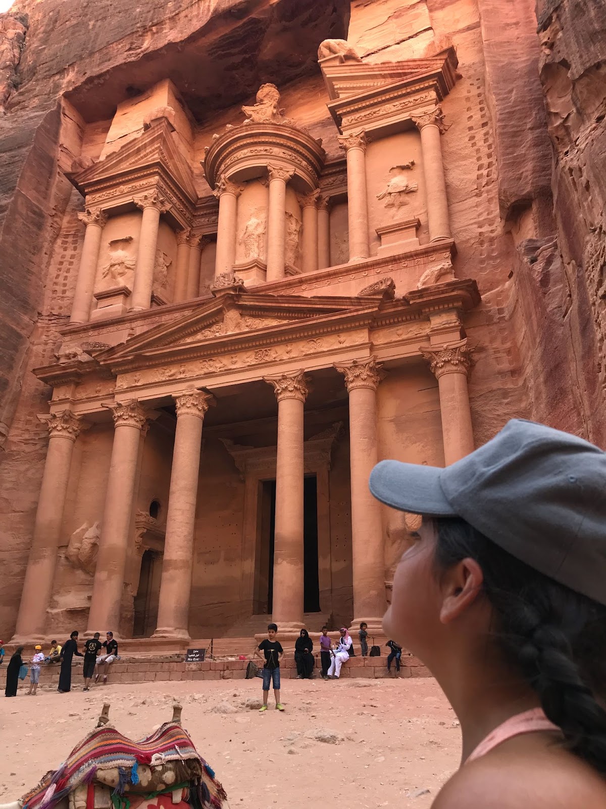 A young woman in a cap looking toward the tall, sand colored pillars of an apparently ancient structure.