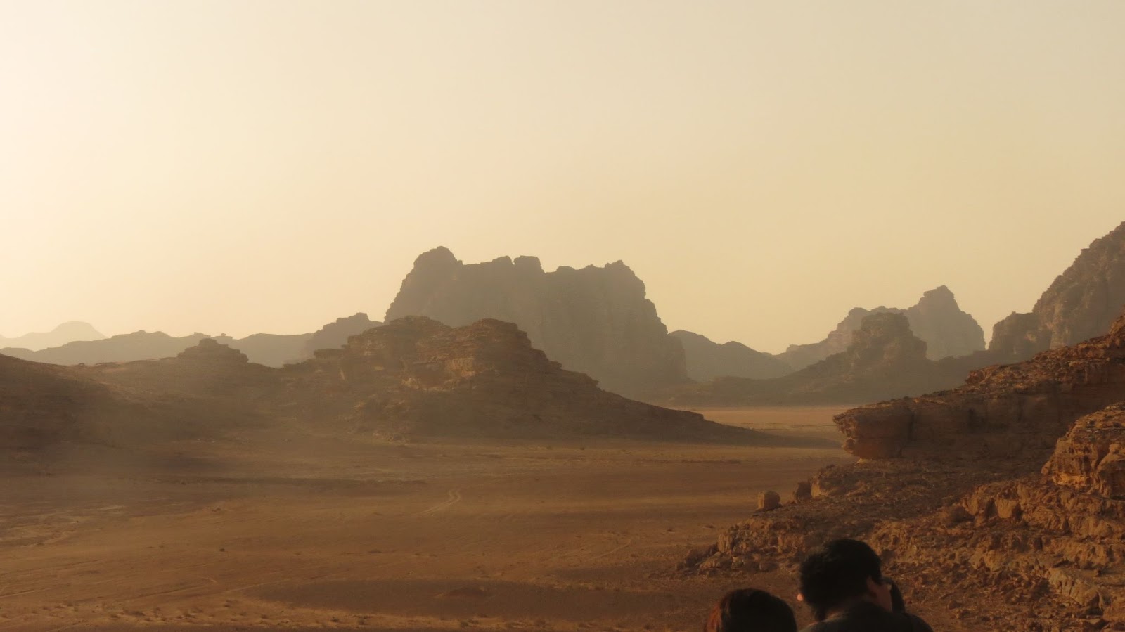 Haze covers a desert landscape of vast sand and rocky structures on the horizon.
