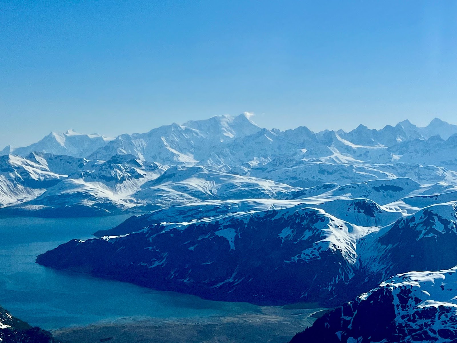 An aerial view of a blue-water bay surrounded by snow-capped mountains.