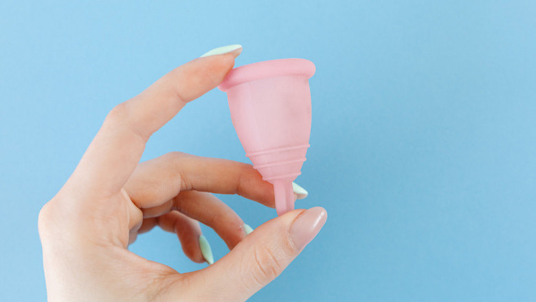 A closeup of a hand holding a pink diva cup against a blue background.