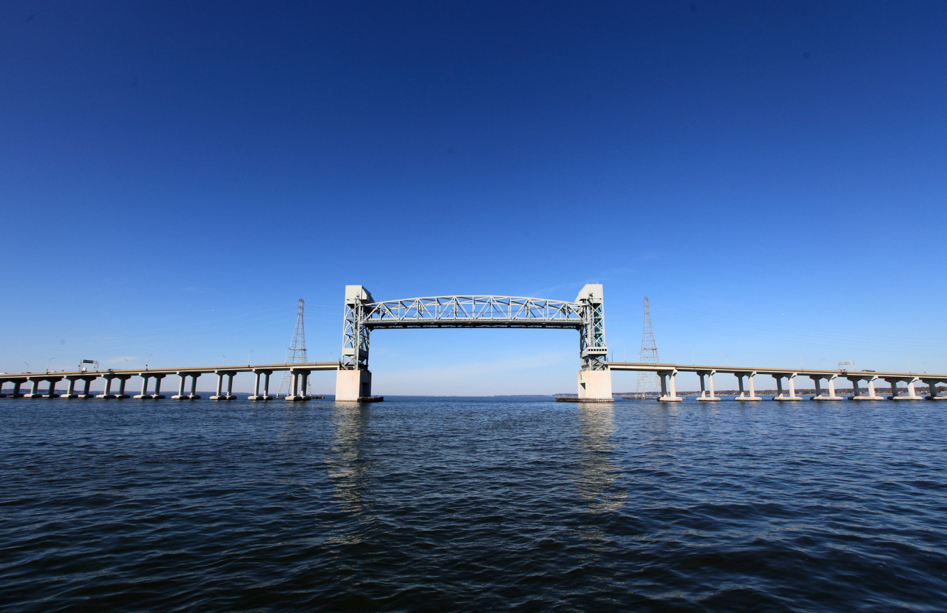 A vertical-lift bridge stretches across a wide river against a blue sky. 
