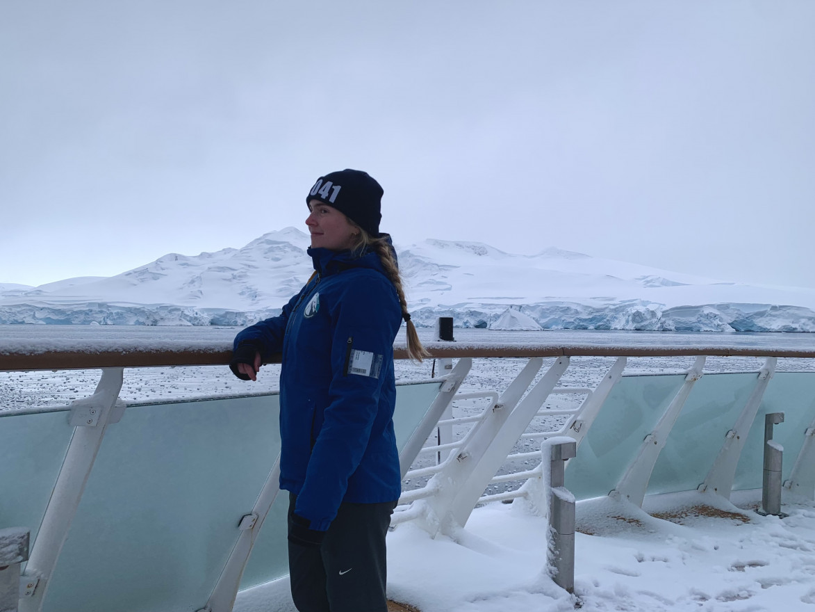 A woman in a blue jacket stands on a snowy ship deck in Antarctica