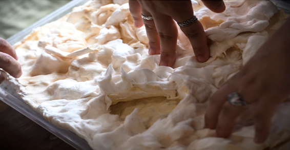 Two hands press into a sheet of fluffy white mycelium