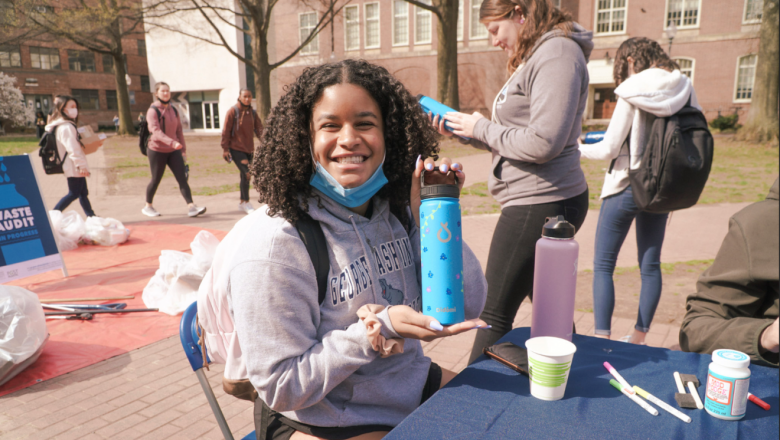 Student in a GW sweatshirt smiles while holding up a decorated blue water bottle.