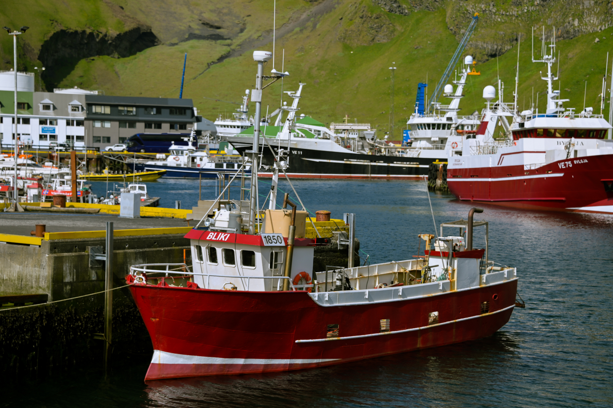 A red fishing boat is docked in a harbor filled with other boats. 