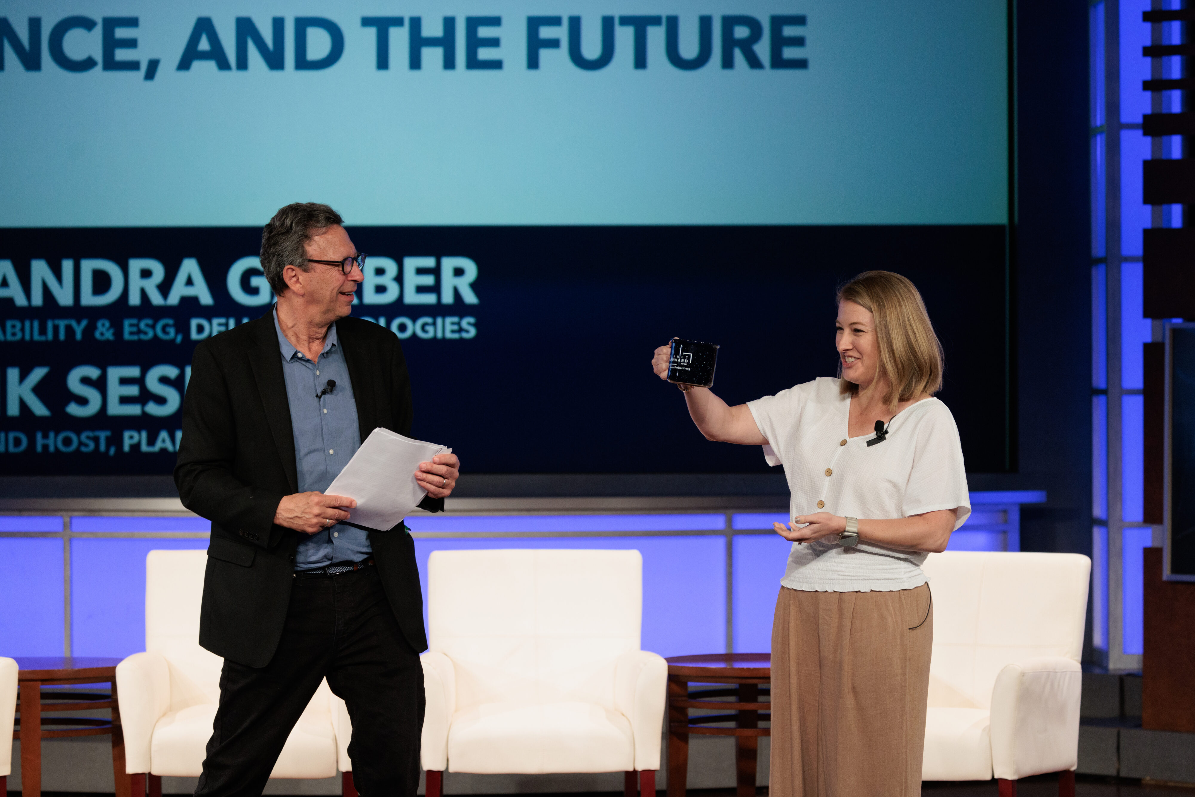 Frank Sesno and Cassandra Garber, VP, Corporate Sustainability & ESG, Dell Technologies; admire a Planet Forward Mug on stage and discuss the role of complexity and science in solving the world's most pressing problems. 