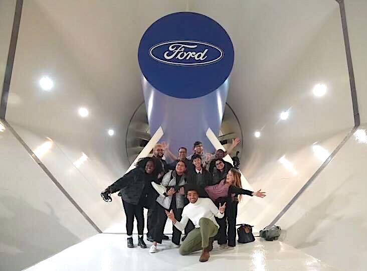 Students and staff pose below a wind tunnel fixture inside a Ford testing facility. 