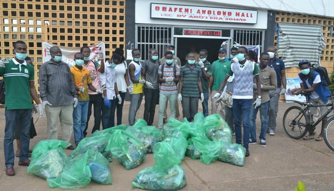 A group of people pose next to a pile of trash bags. 