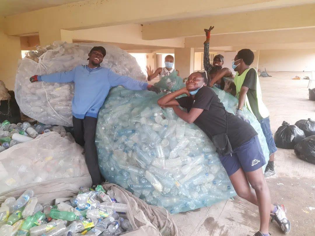 A group of people pose next to several huge bags of plastic bottles. 