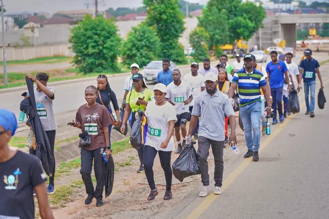 A group of people walk along a road carrying trash bags while plogging.