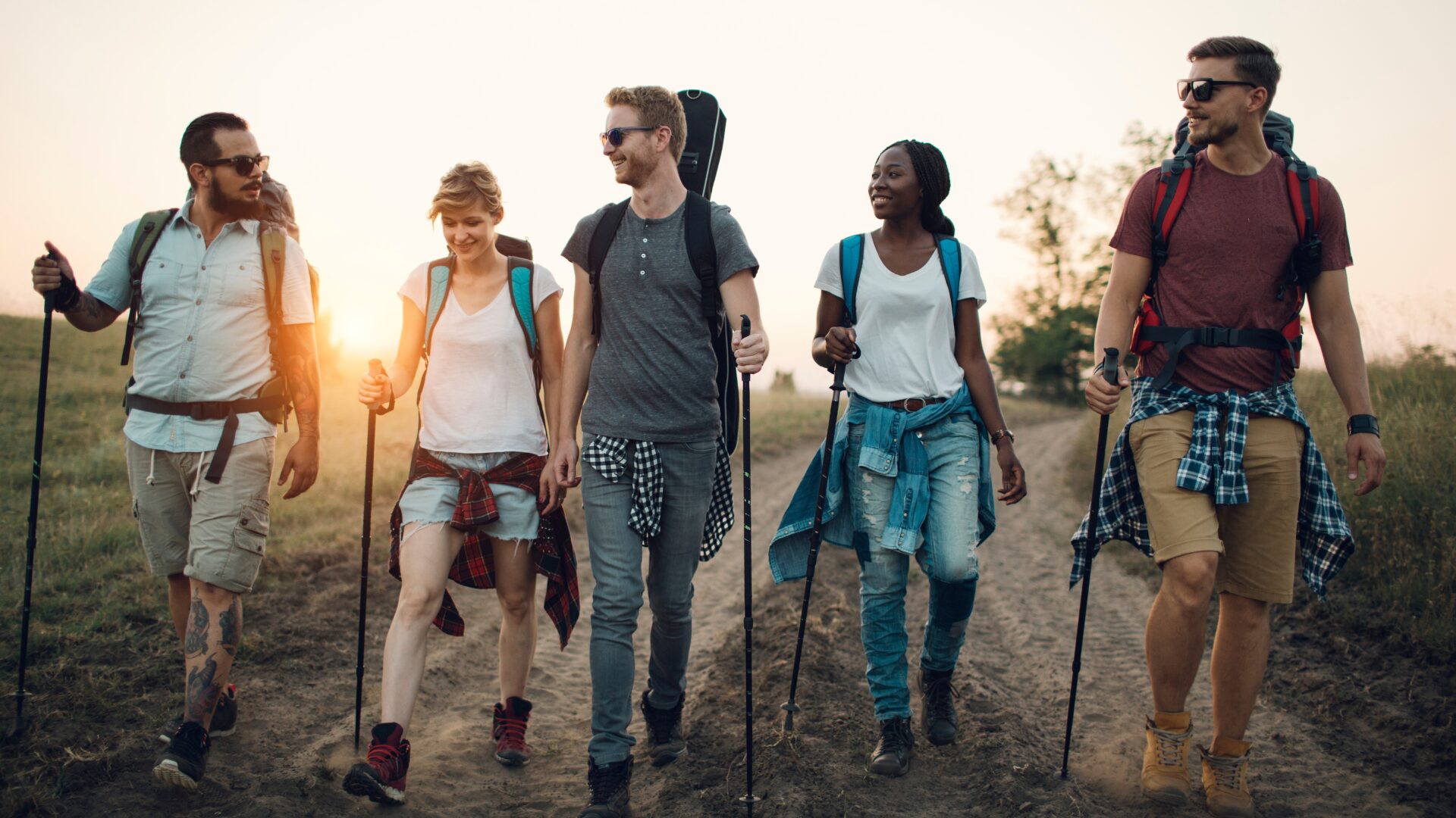 A group of five diverse young people hike in nature while the sun is setting.