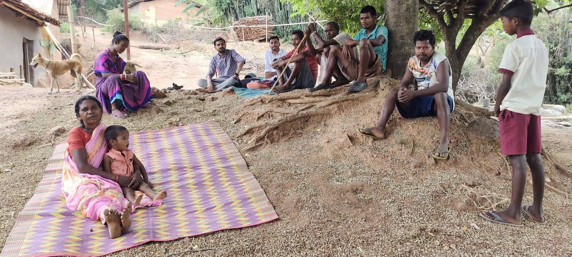 People sitting on the ground near a tribal hamlet.