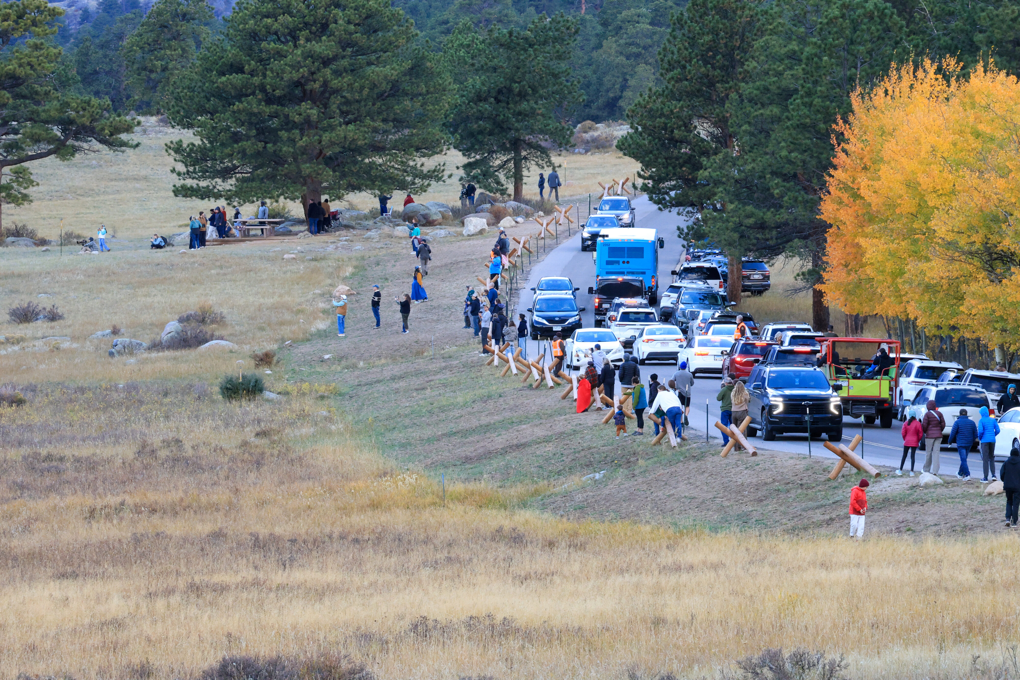 A line of cars and spectators on a rural road.