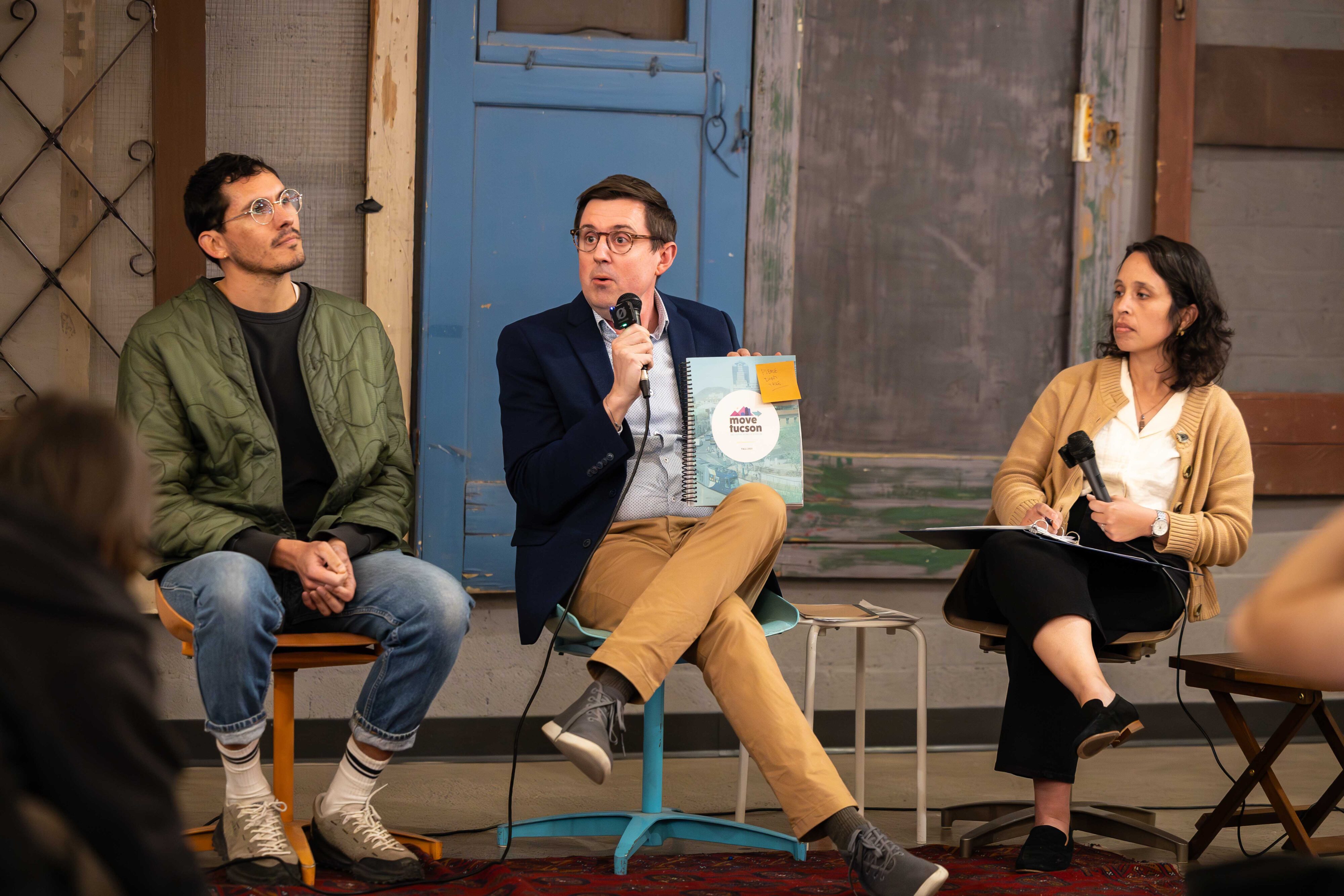 Three panelists, one of whom holds a microphone and book.